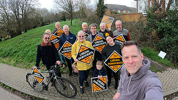 A group of Liberal Democrat team councillors and volunteers, holding up stakeboards, taking a selfie. This represents the menu link to the "Our Councillors" page