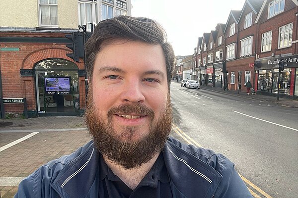 Image of the head and shoulders of candidate Andrew Stevens, standing in the foreground with the high street in the background